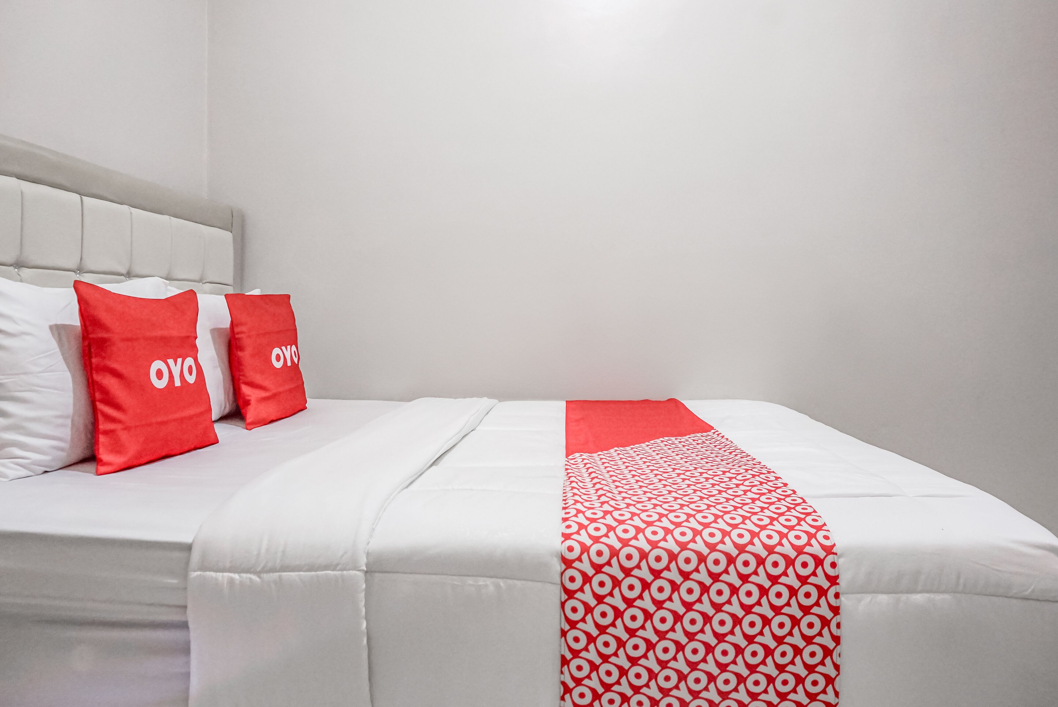 A bed with white bedding and red pillows, a white headboard, and a red and white patterned throw blanket.