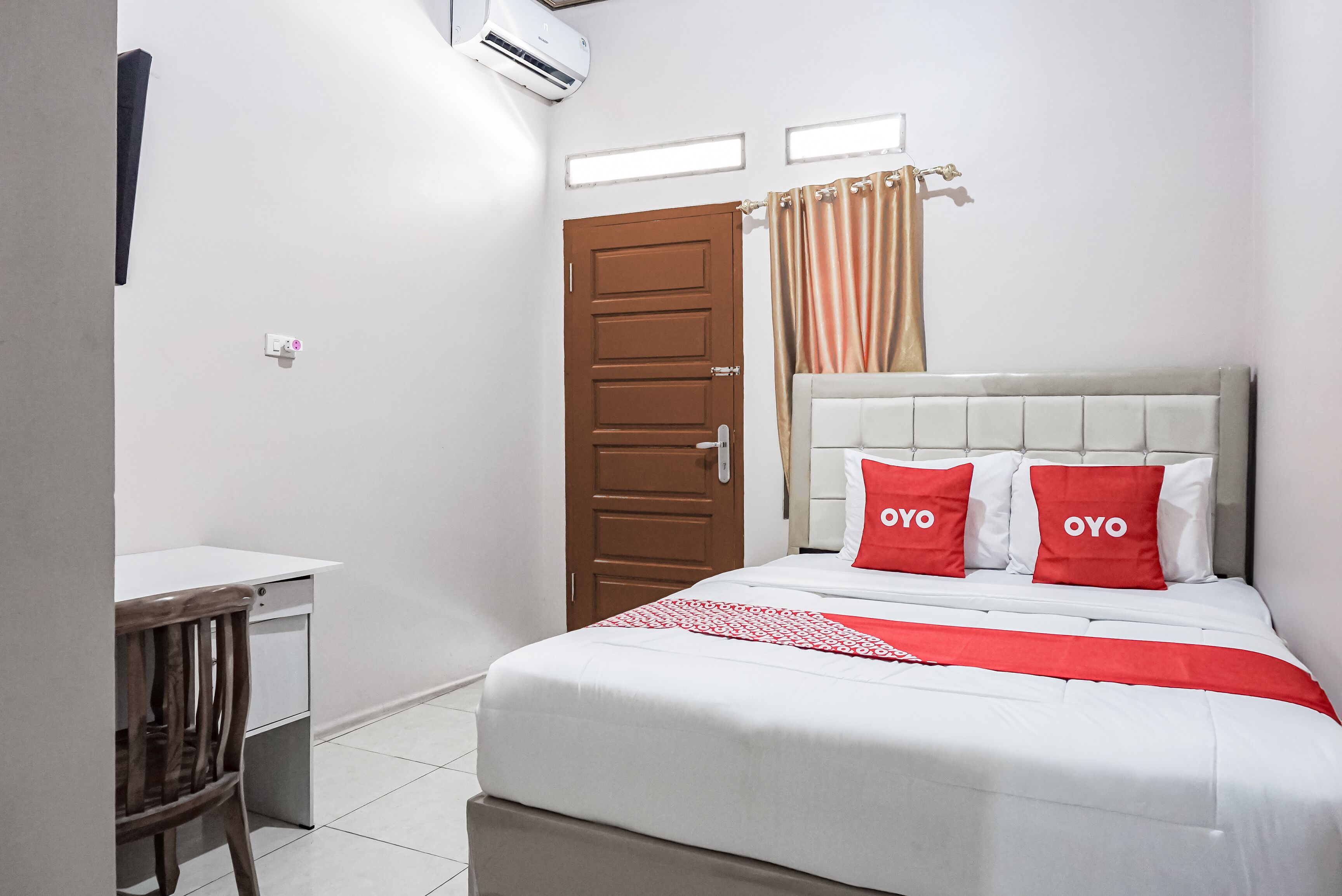 A hotel room with a bed, a desk, a chair, a door, and a window with curtains.