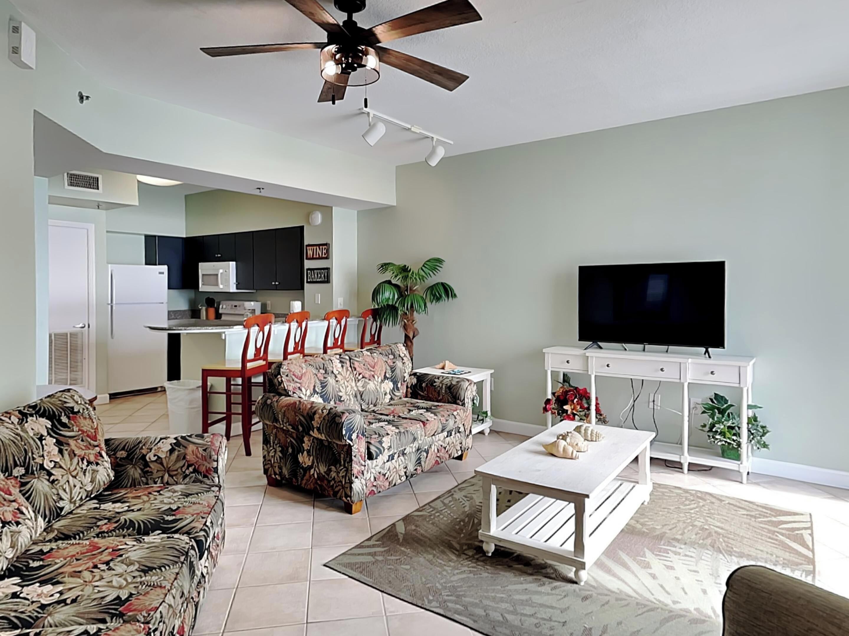 A living room with a sofa, coffee table, TV, and a ceiling fan.