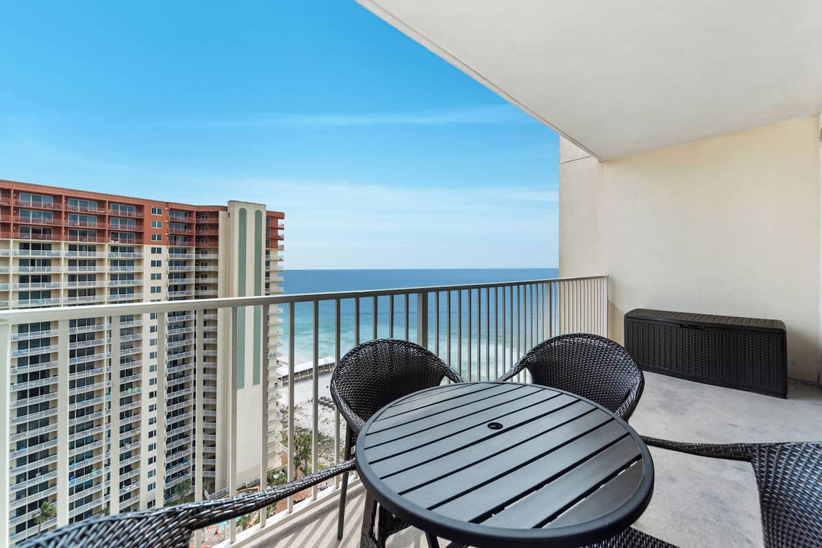 A balcony with a table and chairs, overlooking a beach and high-rise buildings.