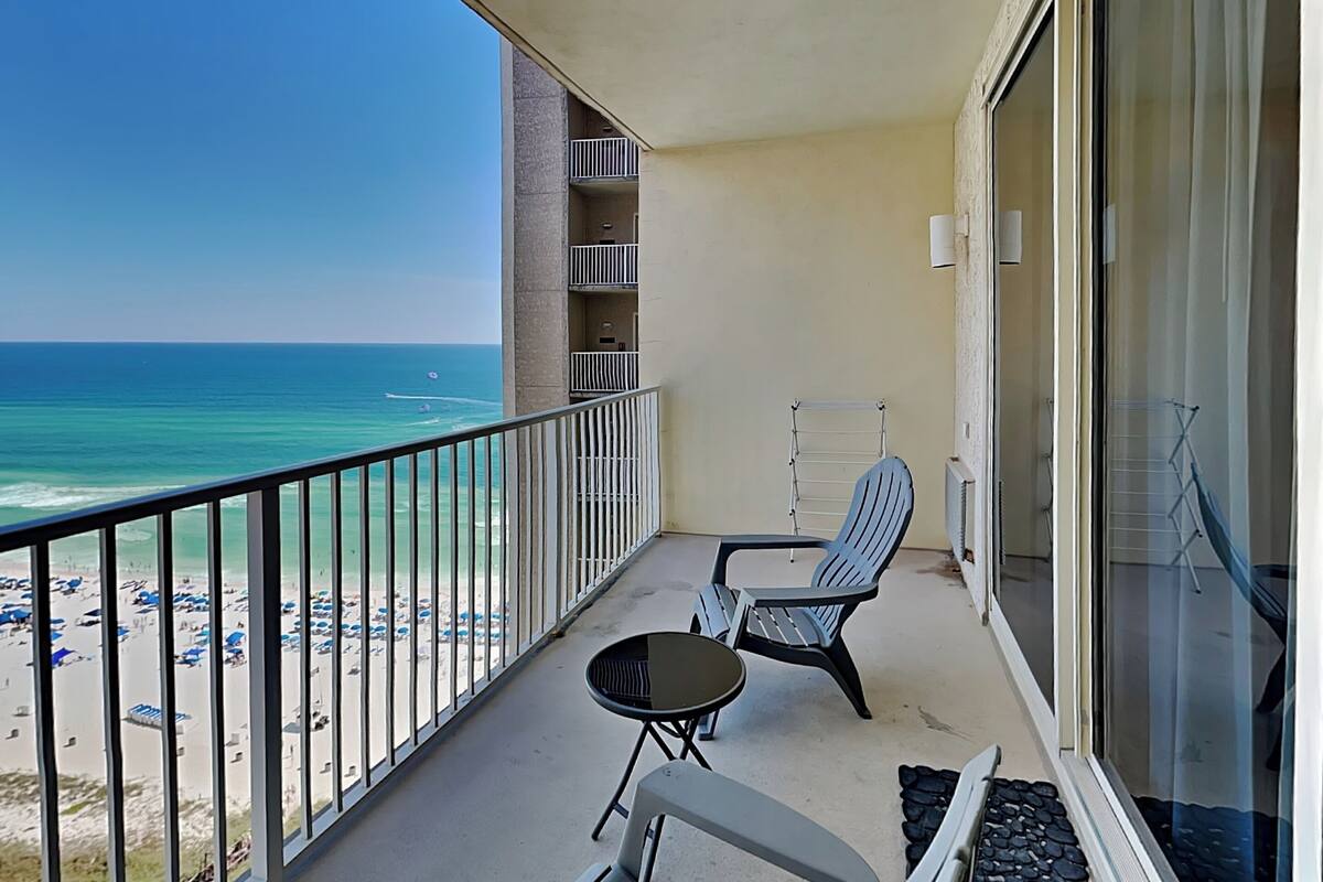 A balcony with a view of the beach and ocean. There are two chairs and a small table.