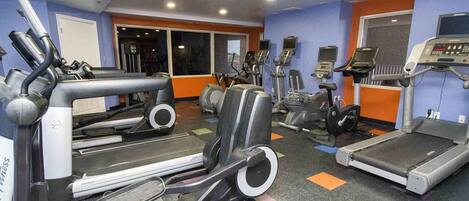 A gym with various cardio machines, including treadmills and elliptical trainers, and a wall-mounted exercise bike.