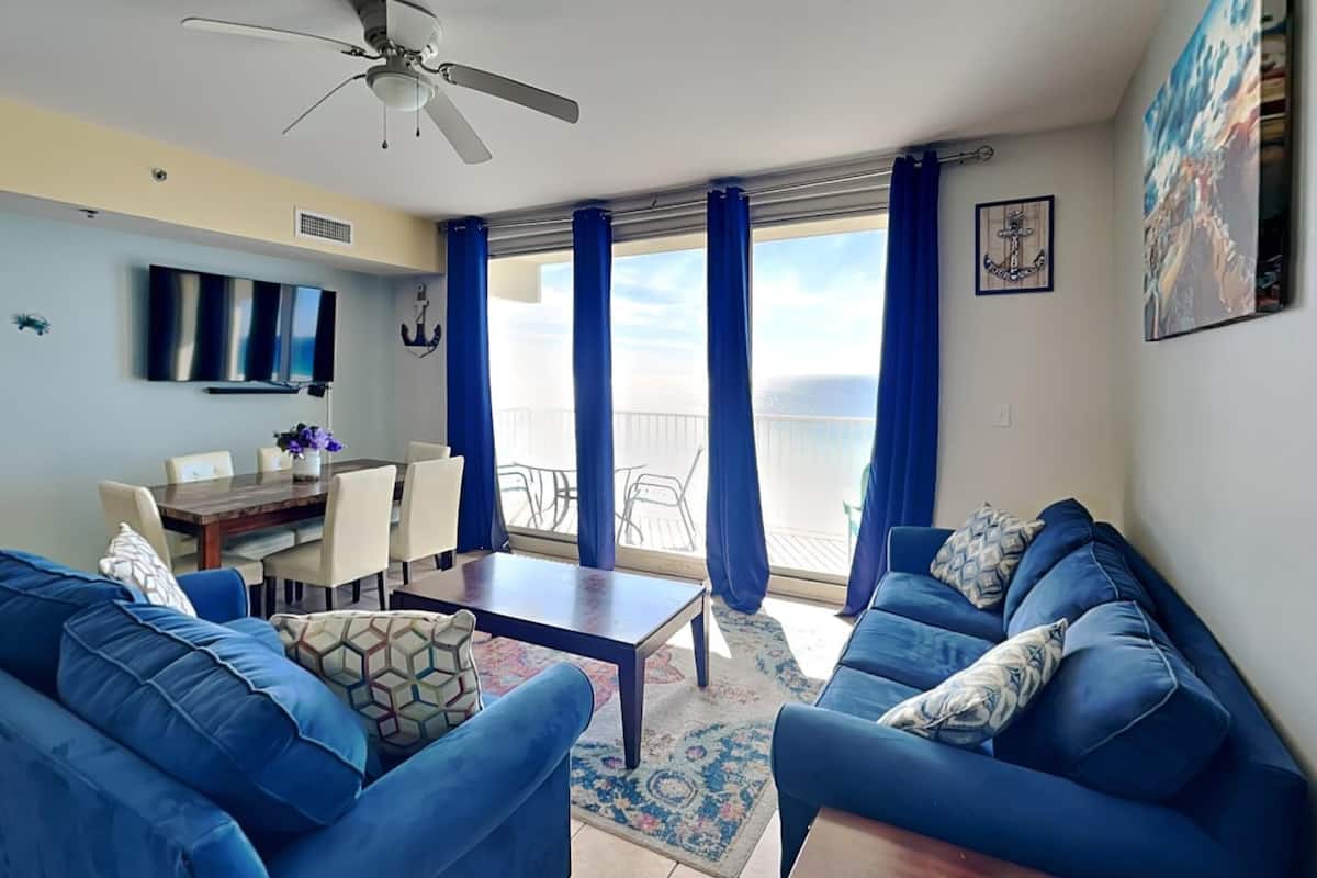 A living room with blue sofas, a dining table, and a ceiling fan.
