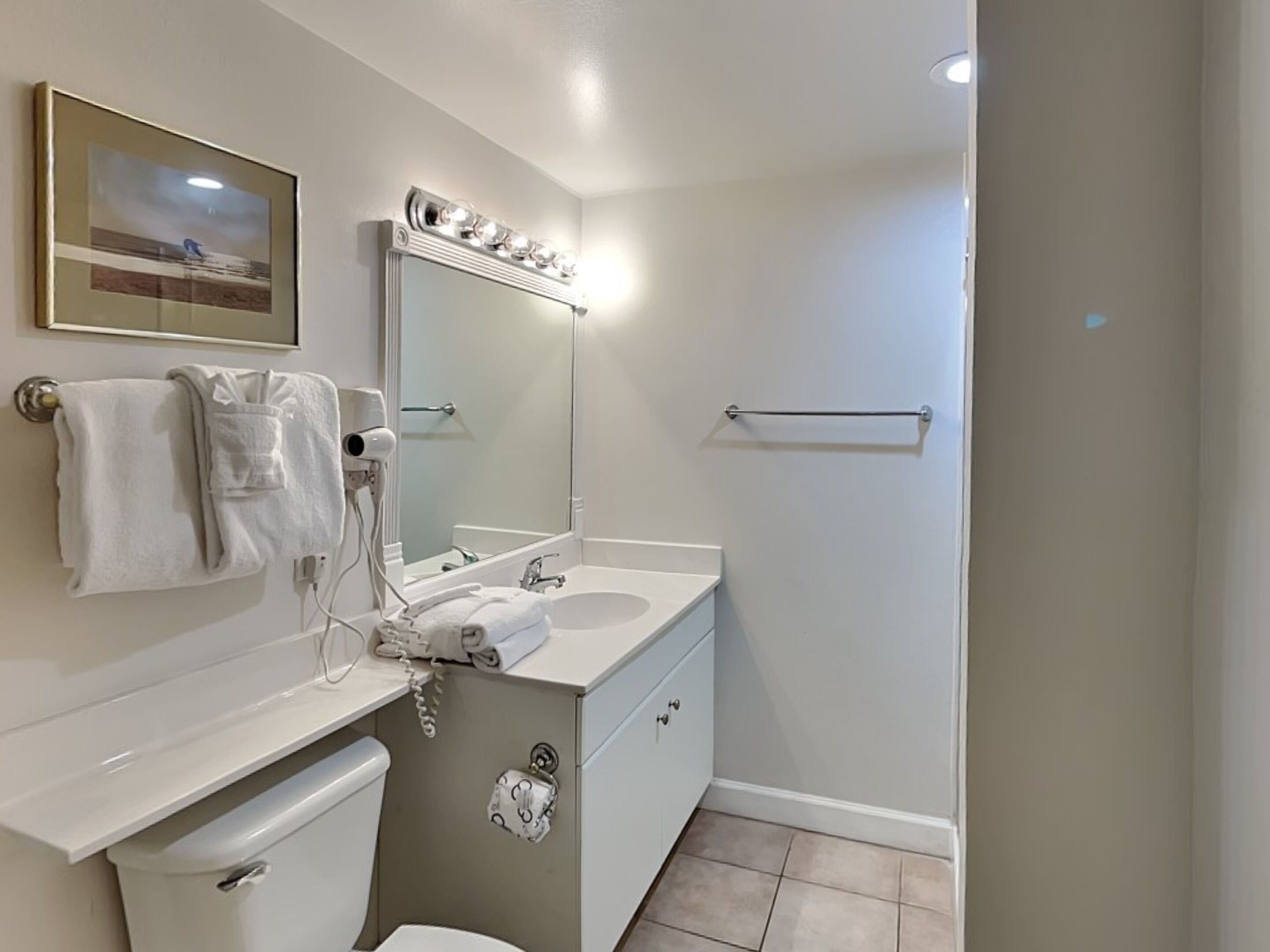A modern bathroom with a white vanity, a large mirror, a towel rack, and a toilet.