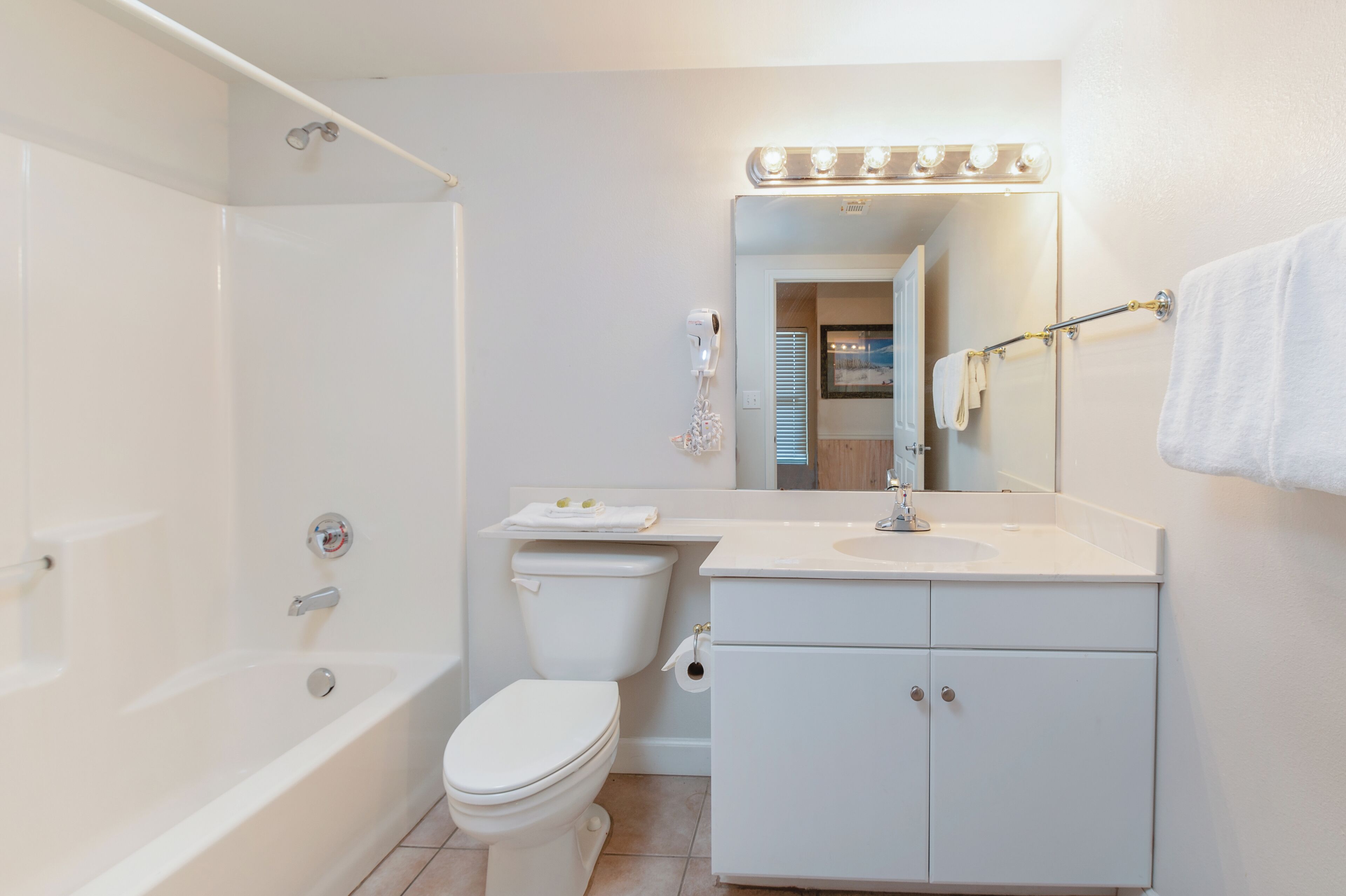 A modern bathroom with a bathtub, toilet, vanity, and a mirror with lights above.