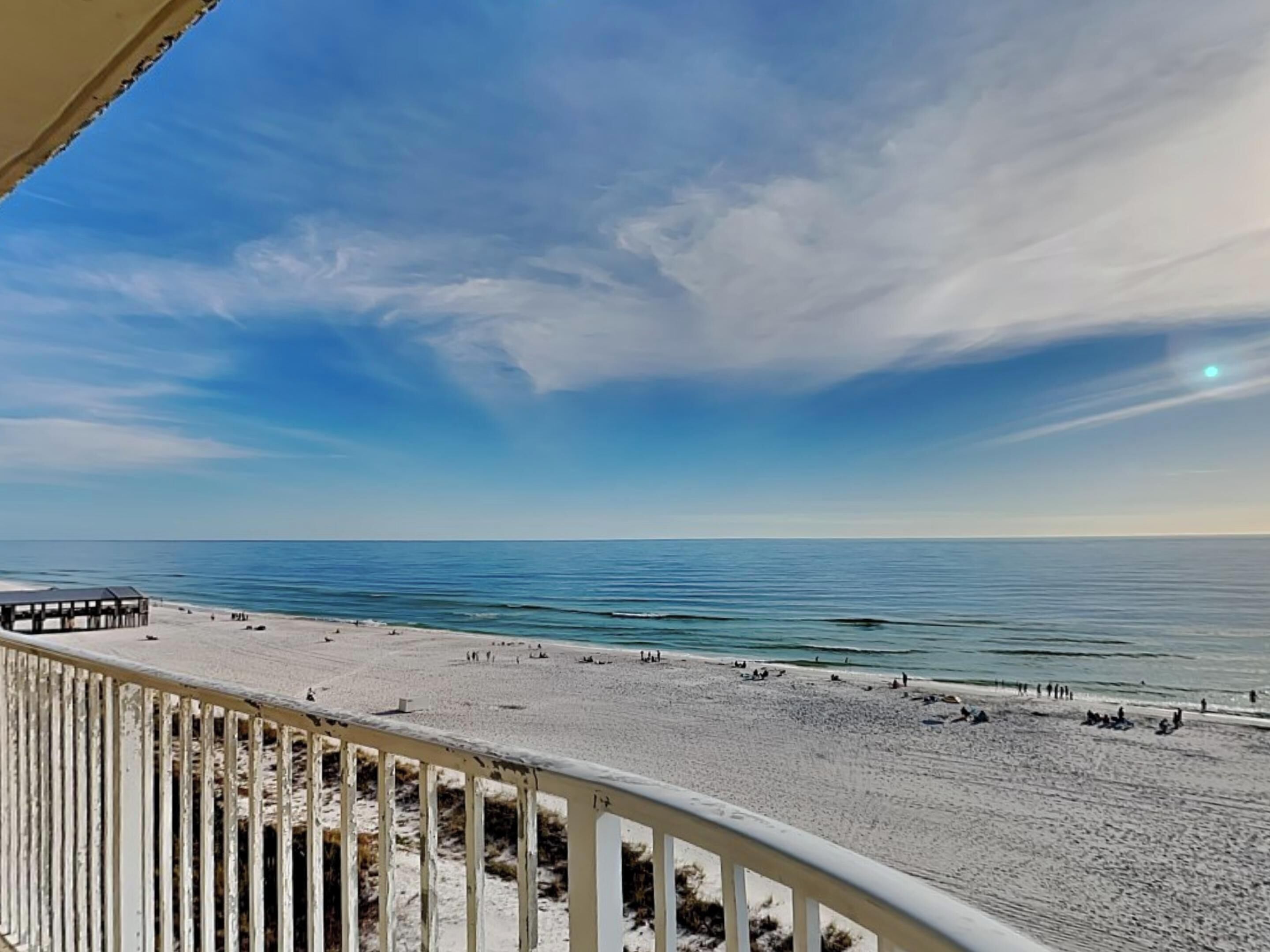 A beach view from a balcony with a railing, a sandy beach, and the ocean.