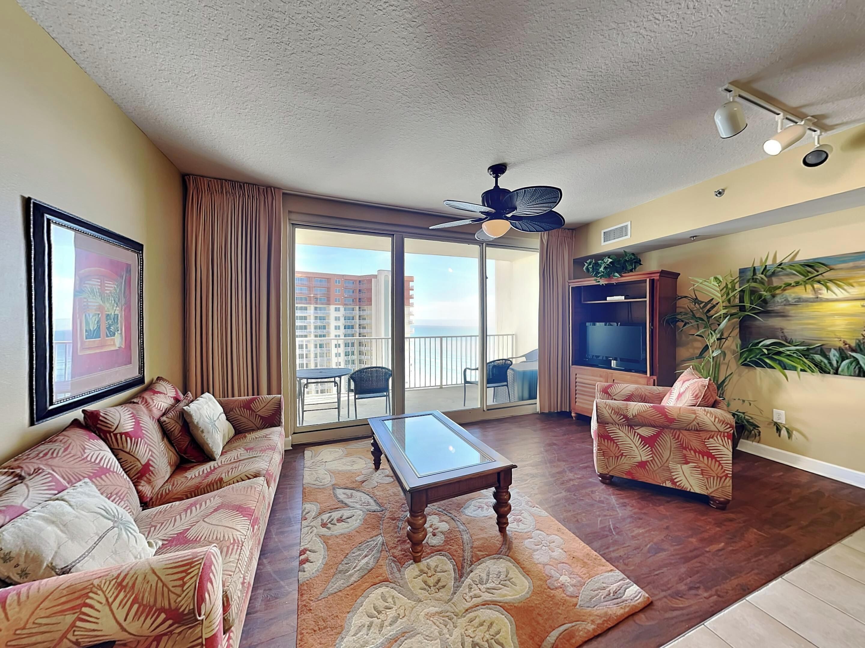 Ein Wohnzimmer mit einer Couch, einem Sessel, einem Couchtisch und einem großen Fenster mit Blick auf Gebäude und einen Balkon.