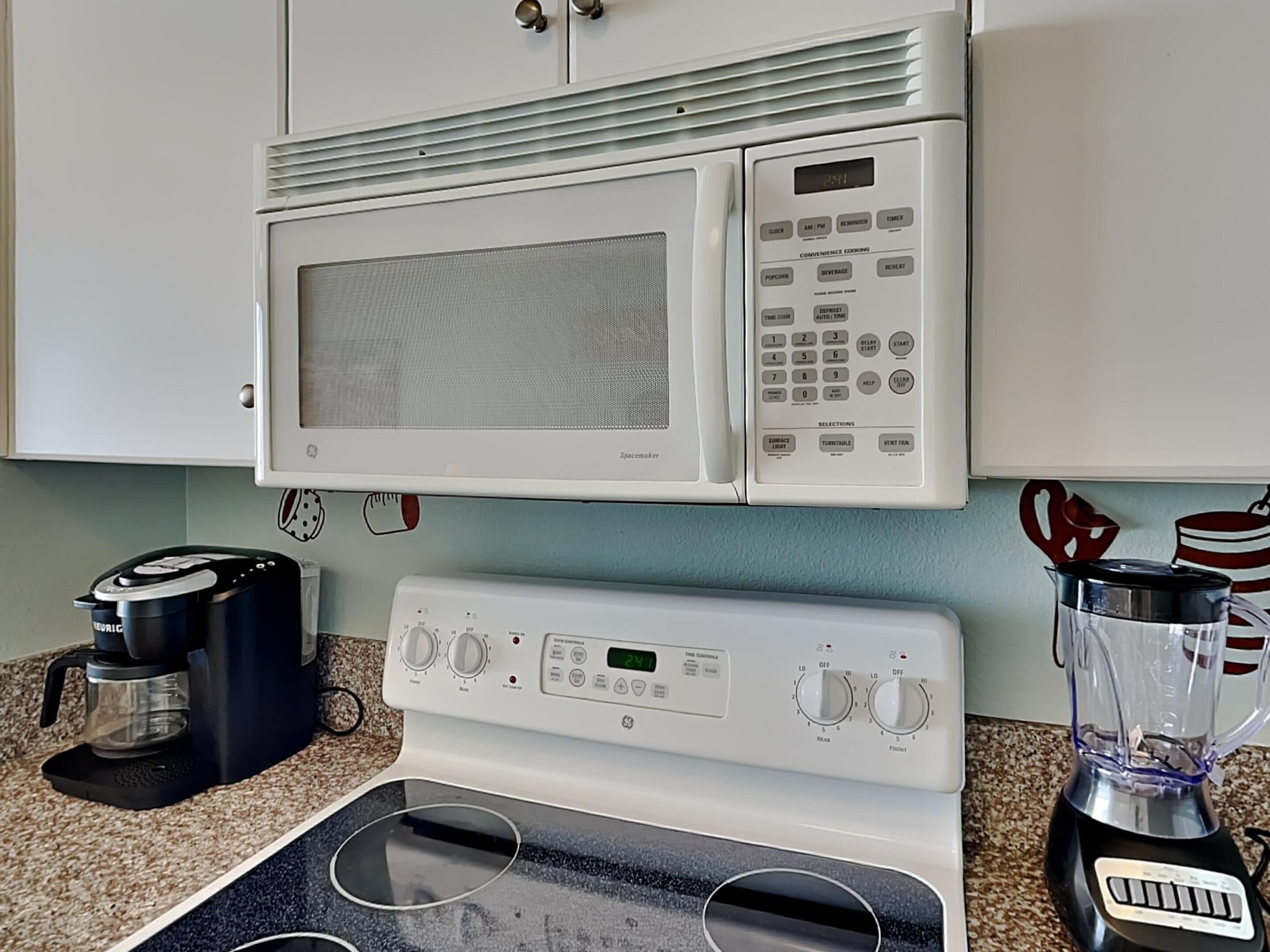 A kitchen with a microwave, stove, coffee maker, and blender.