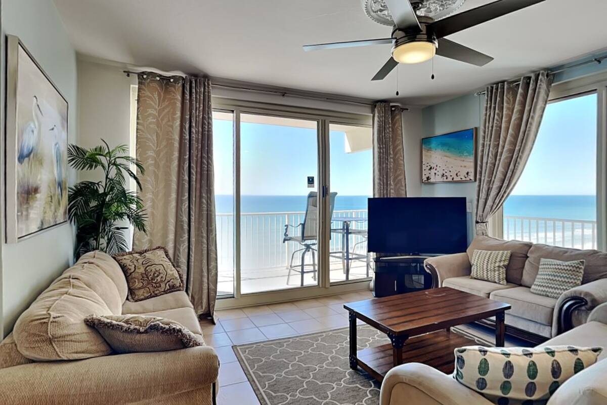 A living room with a large TV, two sofas, a coffee table, and a ceiling fan.