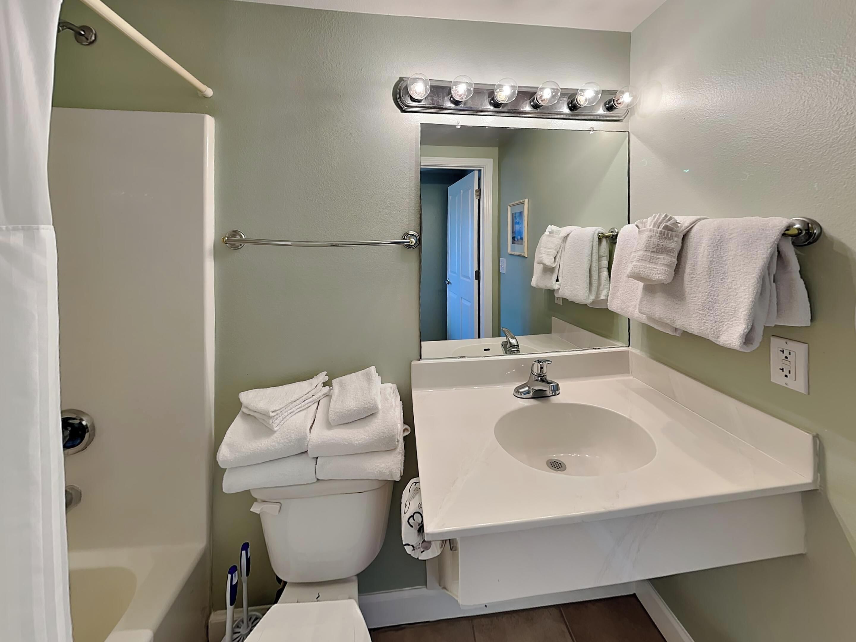 A bathroom with a white sink, a mirror with lights, a towel rack, and a toilet.