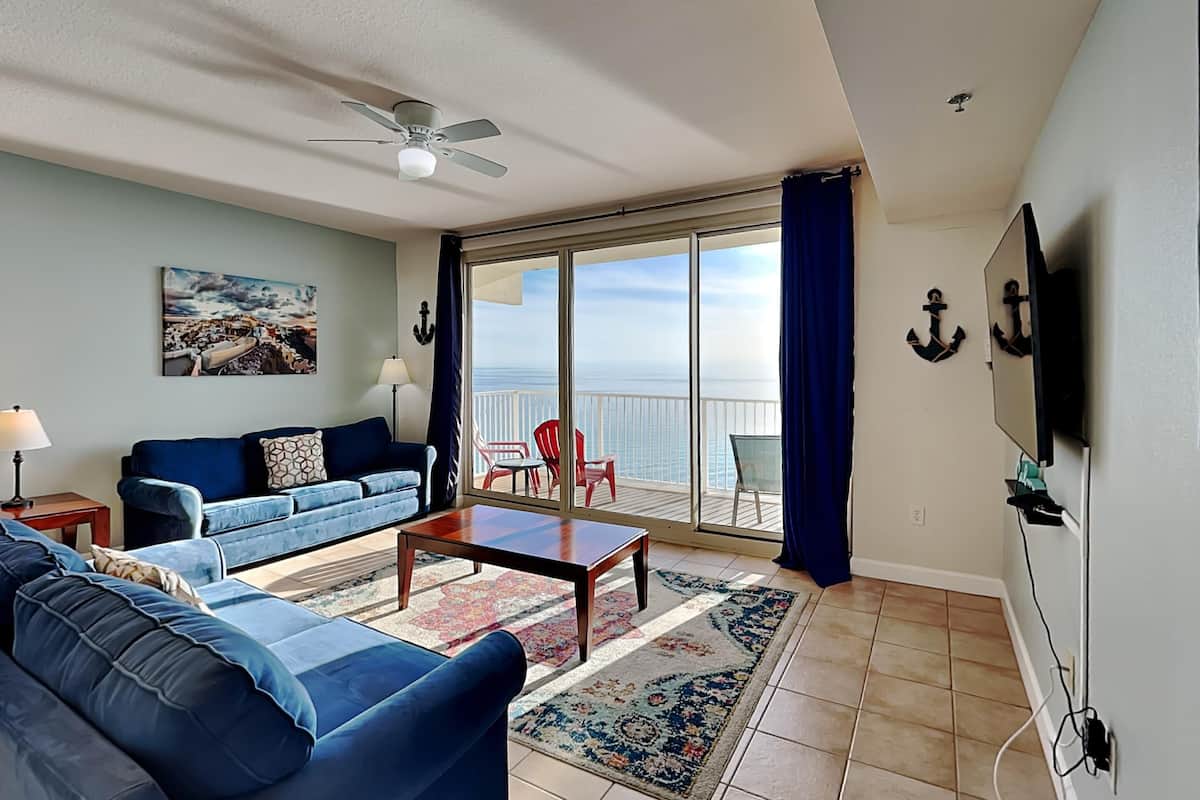 A living room with a sofa, coffee table, and a view of the sea through large sliding glass doors.