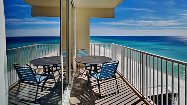 A balcony with a table and chairs, overlooking a clear blue ocean. - Shores of Panama III by Resort Collection (Panama City Beach)