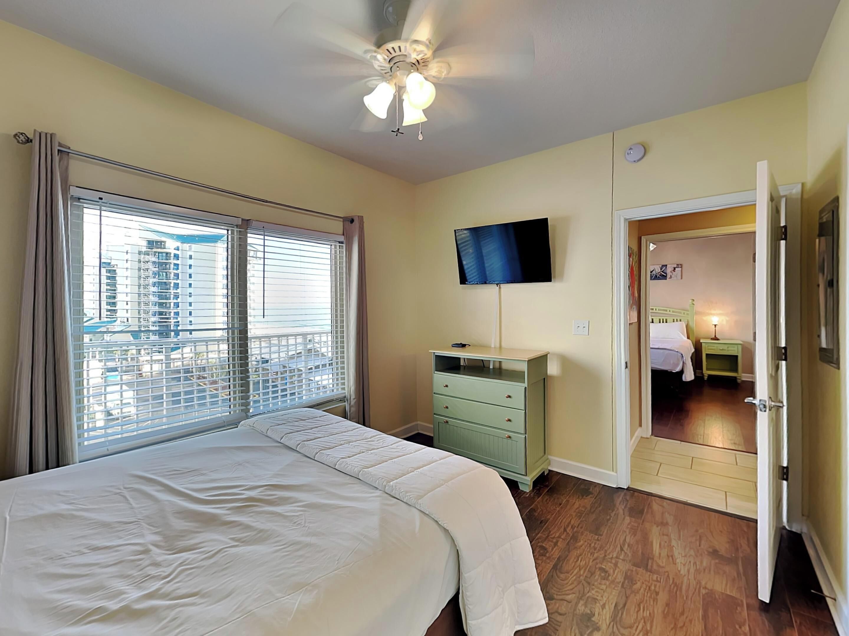 Ein Hotelzimmer mit Bett, Fernseher, Schminktisch und einem Balkon mit Blick auf die Stadt.