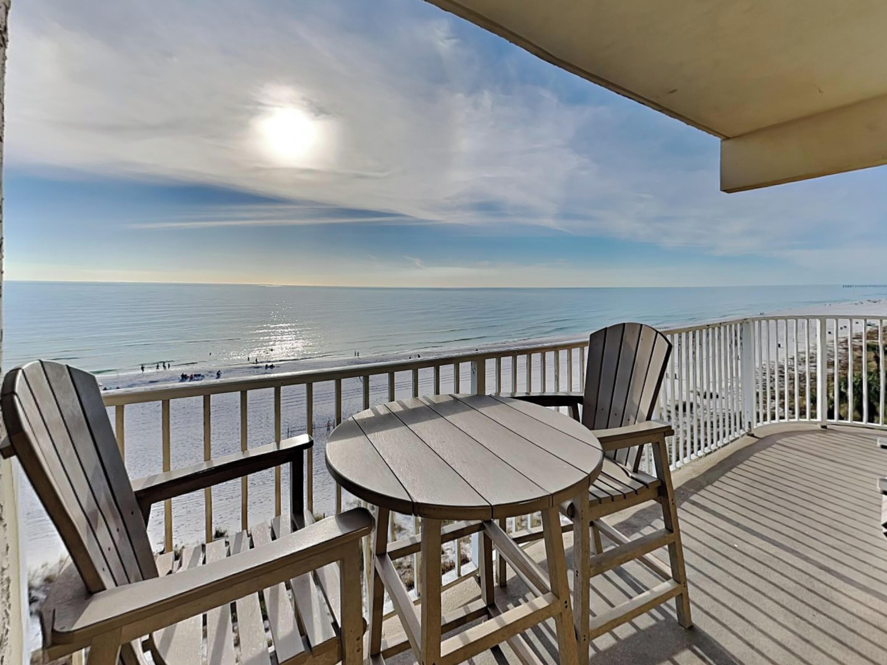 Um deck de madeira com uma mesa e duas cadeiras, com vista para a praia.