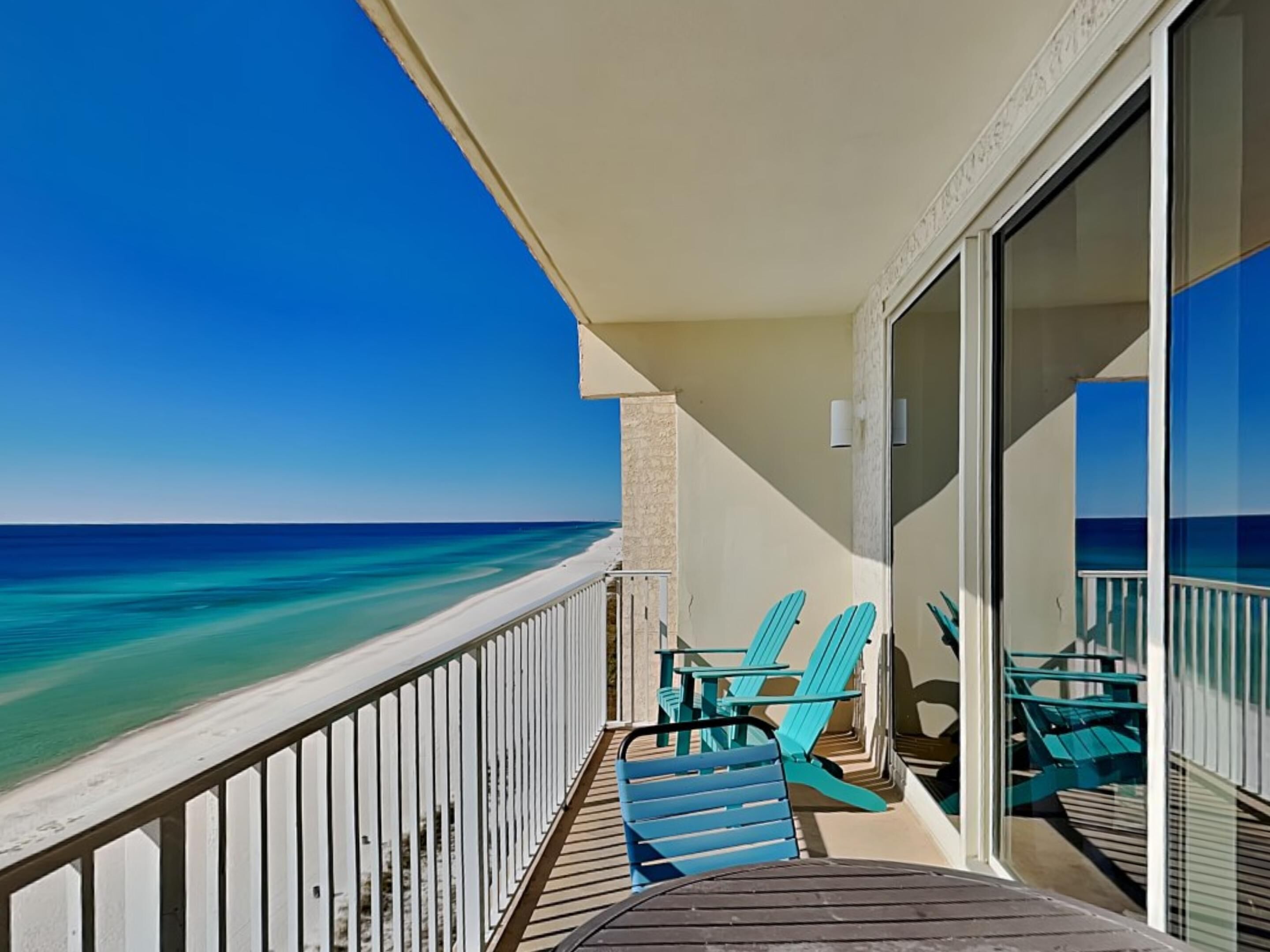 A balcony with a view of the ocean, featuring a wooden deck and turquoise chairs.