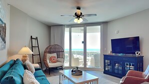 A living room with a blue sofa, a wicker chair, a white coffee table, a TV on a cabinet, and a balcony with a view. - The Palms of Destin by Southern Vacation Rentals (Destin)