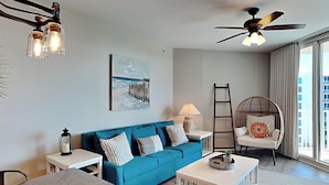 A modern living room with a blue sofa, a white coffee table, a wooden dining table, and a ceiling fan. - The Palms of Destin by Southern Vacation Rentals (Destin)