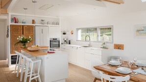 Een moderne keuken met witte kasten, een houten eiland en een eethoek met witte stoelen.