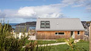 Een modern huis met een grijs dak, houten wanden en uitzicht op zee.