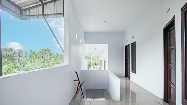 A modern hallway with white walls, a tiled floor, and a large window offering a view of greenery. - Hotel O Owo Guest House Syariah (Jambi)
