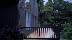 A modern two-story building with a dark exterior, a wooden deck, and a view of the surrounding greenery. - Private Cottage minutes from Moraine State Park and McConnell's Mill State Park. (Portersville)