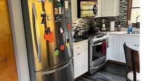 A kitchen with a stainless steel refrigerator, white cabinets, a stone backsplash, and a dark wood floor. - Private Cottage minutes from Moraine State Park and McConnell's Mill State Park. (Portersville)