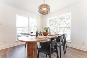 A dining area with a wooden table, black chairs, a woven pendant light, and large windows with a view of trees. - Secluded Hill Country Luxe: Vibes, Pool, Best Spot (Austin)