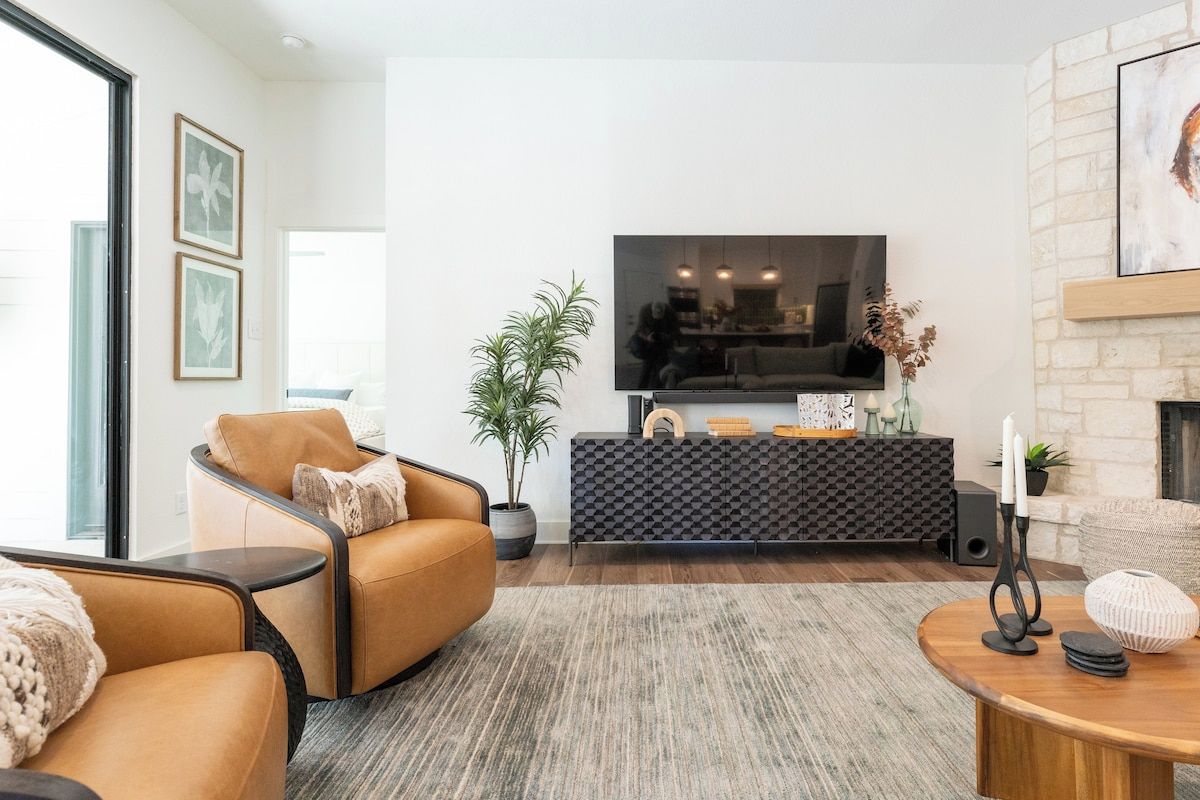 A modern living room with a leather sofa, a flat-screen TV, a fireplace, and a decorative plant.
