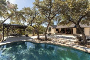 A swimming pool with a pergola and outdoor seating area, surrounded by trees and a house with a patio. - Secluded Hill Country Luxe: Vibes, Pool, Best Spot (Austin)