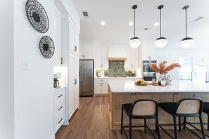 A modern kitchen with white cabinetry, a large island, and pendant lighting. - Secluded Hill Country Luxe: Vibes, Pool, Best Spot (Austin)