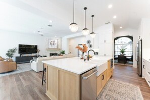 A modern kitchen with a large island, pendant lighting, and a dining area with a view. - Secluded Hill Country Luxe: Vibes, Pool, Best Spot (Austin)