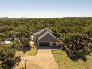 A single-story house with a garage, surrounded by trees and a clear sky. - Secluded Hill Country Luxe: Vibes, Pool, Best Spot (Austin)
