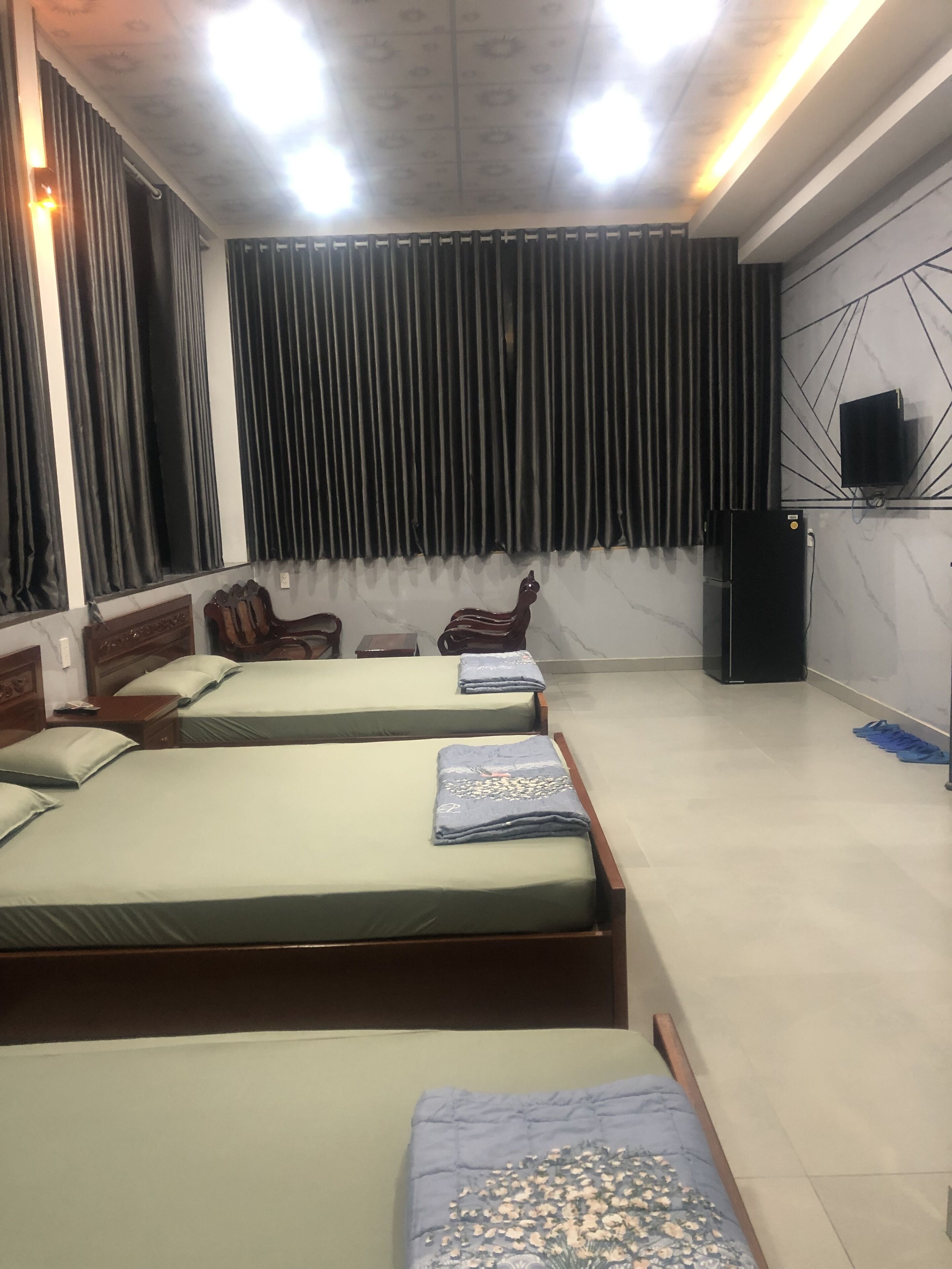 A hotel room with three beds, a wooden headboard, a black refrigerator, and a wall-mounted TV.