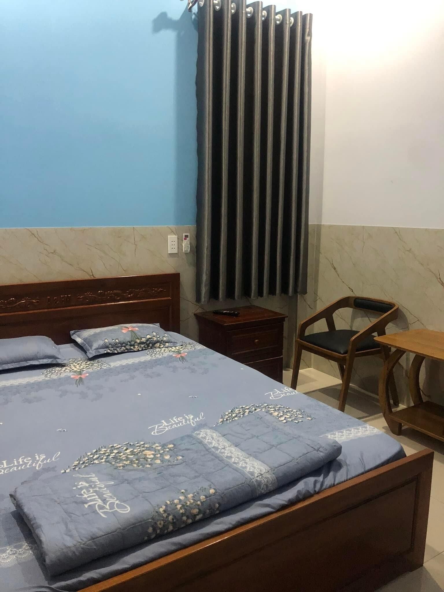 Un dormitorio con cama, mesita de noche de madera, una silla y una pequeña mesa.