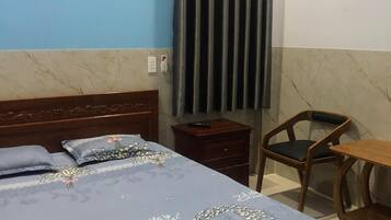 Un dormitorio con cama, mesita de noche de madera, una silla y una pequeña mesa.