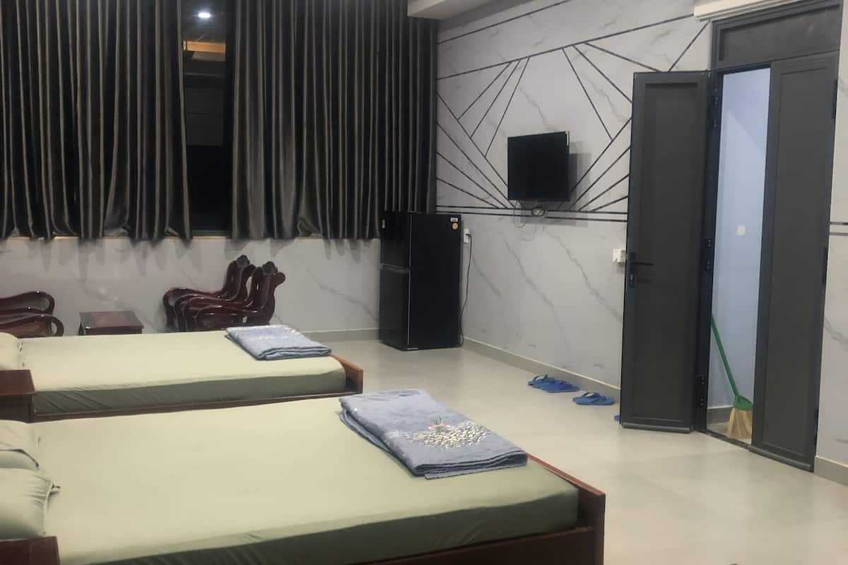 Ein Hotelzimmer mit zwei Betten, einem Flachbildfernseher, einem Deckenventilator und einer Tür.