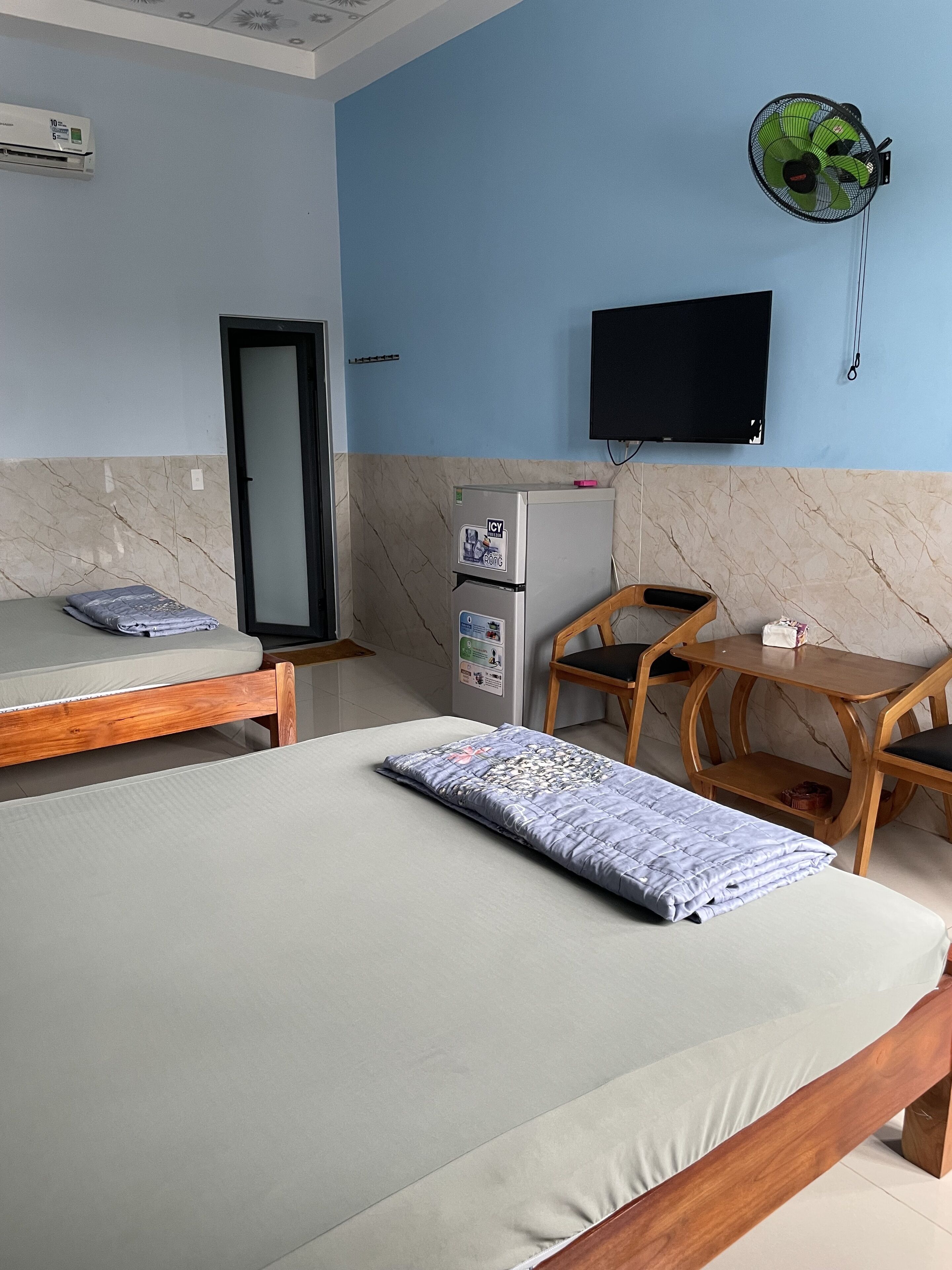 Un dormitorio con cama, escritorio, silla, refrigerador y televisor montado en la pared.