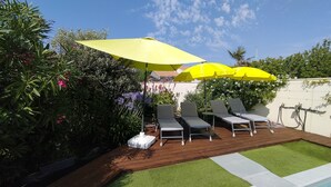 Um quintal com piscina, deck de madeira e três cadeiras de descanso sob guarda-sóis amarelos.