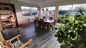 Uma sala de jantar espaçosa com uma mesa de madeira e cadeiras de vime, grandes janelas com vista para o exterior e uma estante embutida.