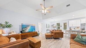 A spacious living room with a large TV, comfortable seating, a ceiling fan, and a kitchen area in the background. - Florida Cottage | Fenced Yard | Its All Good | Santa Rosa Beach (Santa Rosa Beach)