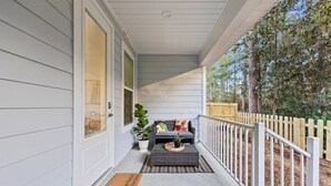 A covered porch with a white railing, a gray sofa with cushions, a small table, and a potted plant. - Florida Cottage | Fenced Yard | Its All Good | Santa Rosa Beach (Santa Rosa Beach)