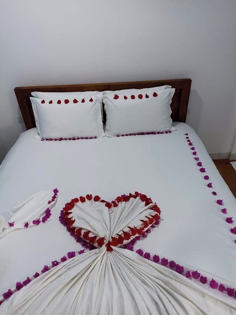 A bed with white bedding and a heart-shaped arrangement of red and purple flowers.