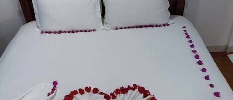 A bed with white bedding and a heart-shaped arrangement of red and purple flowers.