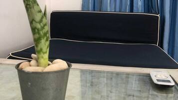A room with a bed, a potted plant, and a remote control on a glass table.