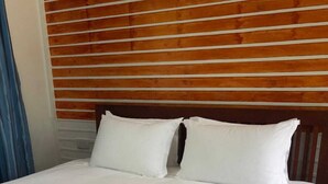 Un lit bien fait, avec des draps blancs et deux oreillers, une tête de lit en bois et une serviette enroulée posée sur le lit.