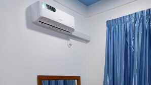 Une pièce avec un bureau en bois, un miroir, un rideau bleu et un appareil de climatisation.