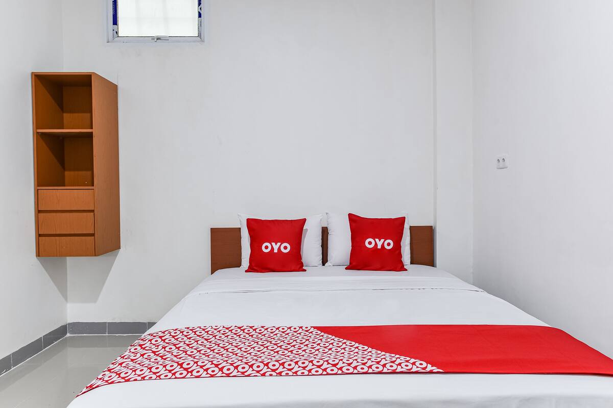 A single bed with two red pillows, a white bedspread, and a red and white patterned blanket.