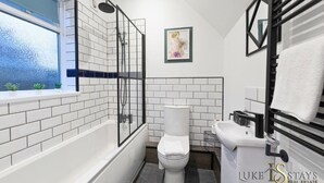 Uma casa de banho moderna com cabine de duche em vidro, azulejos brancos, sanita e lavatório.