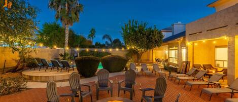 An outdoor patio with a fire pit, lounge chairs, and ambient lighting.