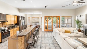 A spacious kitchen with a central island, a dining area with bar stools, and a living room with a sofa and fireplace. - Luxury 5 Bedroom Scottsdale Home with Heated Pool! (Scottsdale)